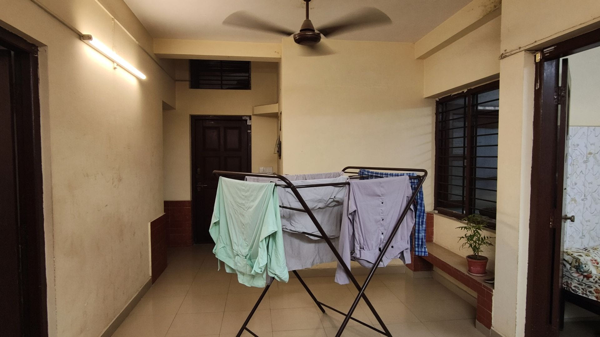 A ceiling fan above an indoor clothes horse of shirts in a tiled Indian hallway