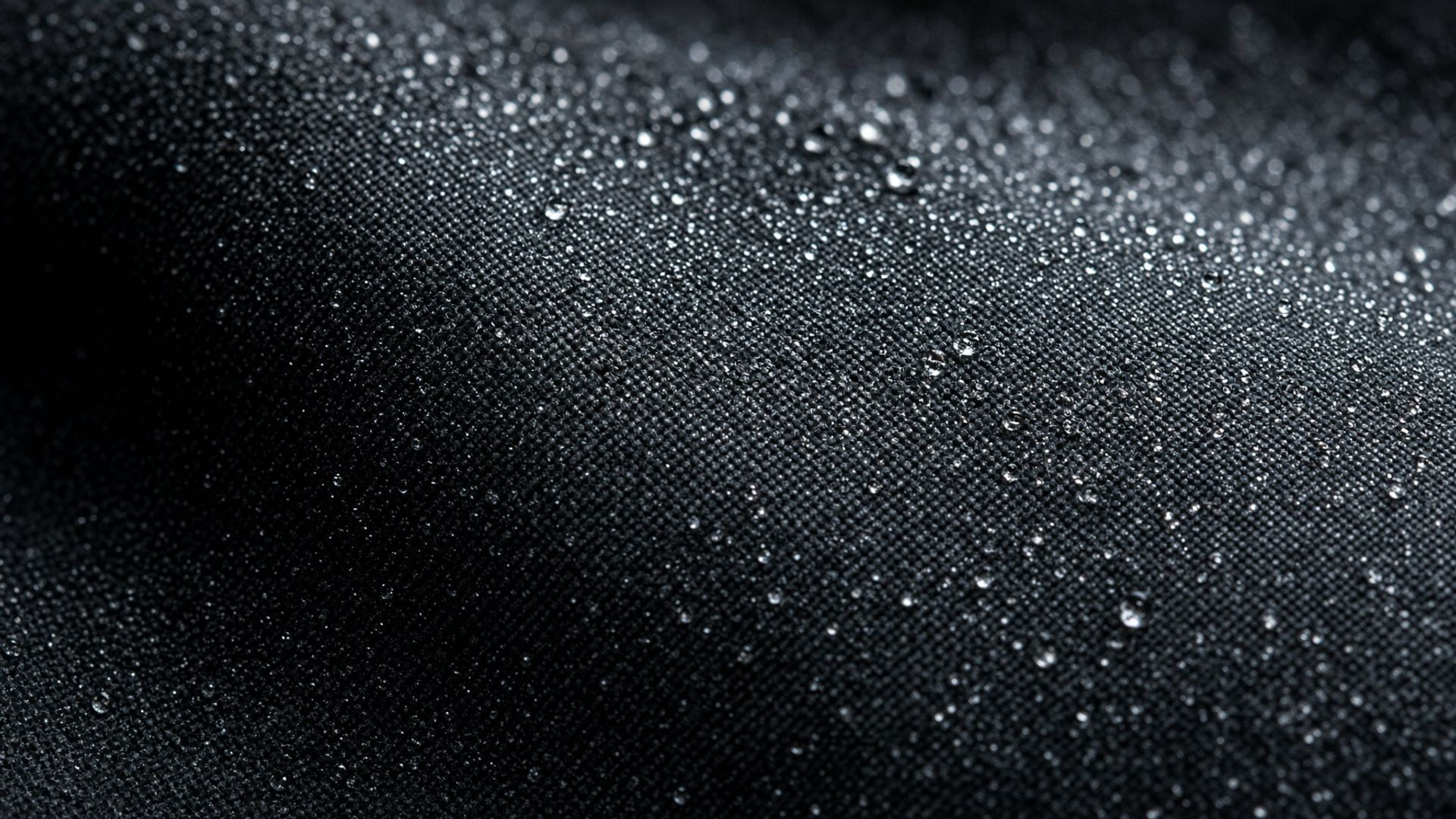 Fine mist droplets settling into the weave of a dark shirt, the contact surface where odor control actually happens