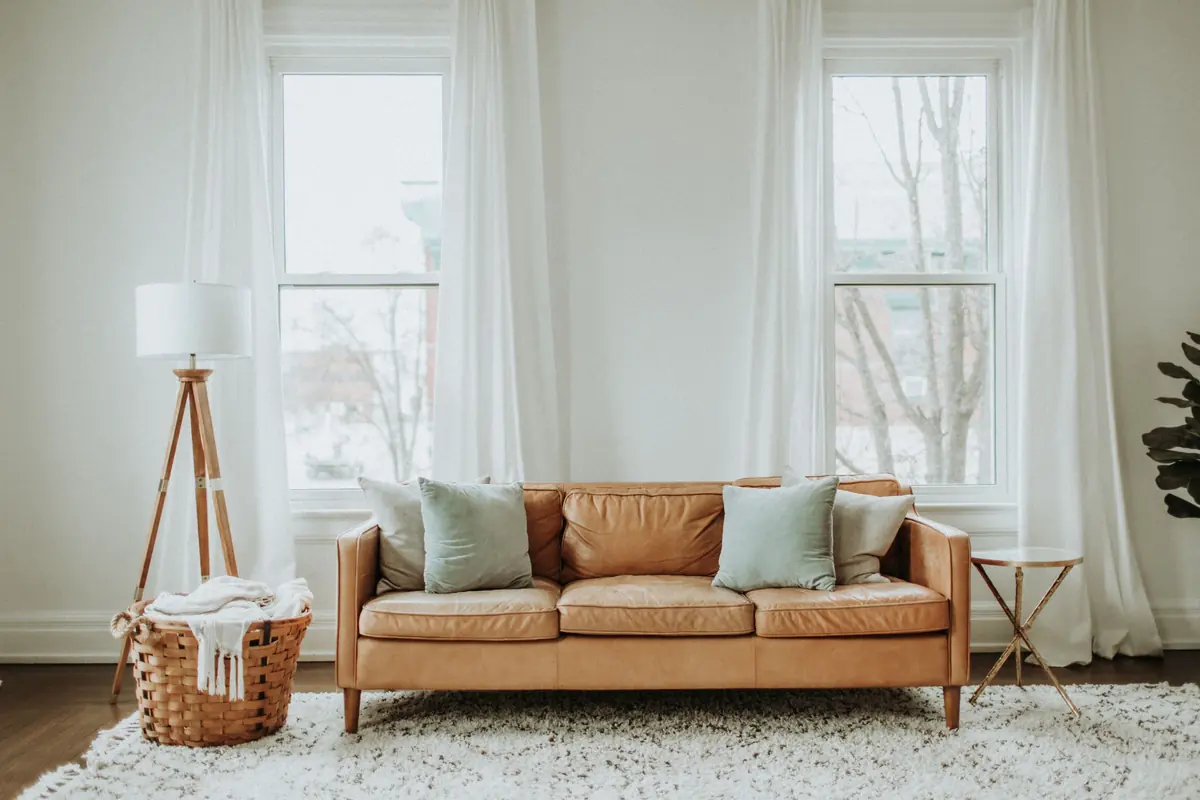 A bright living room with a leather sofa, cushions and long curtains