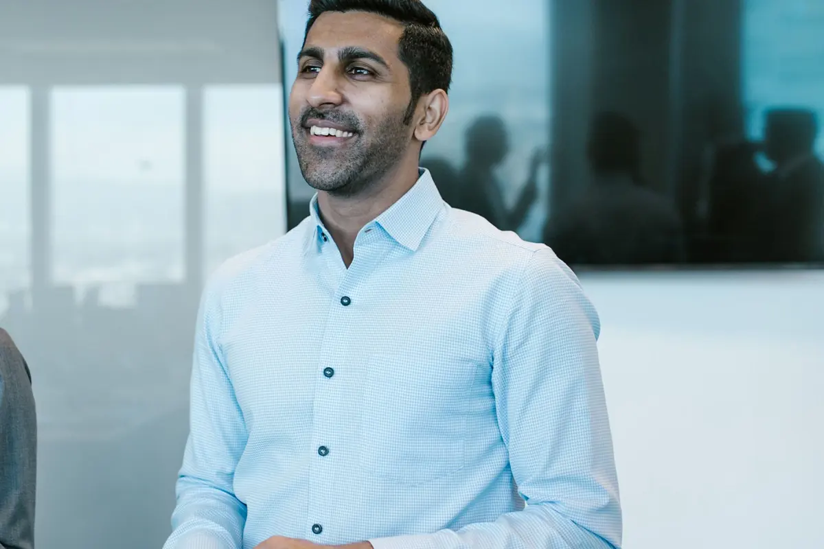 A smiling man in a light blue office shirt presents to colleagues