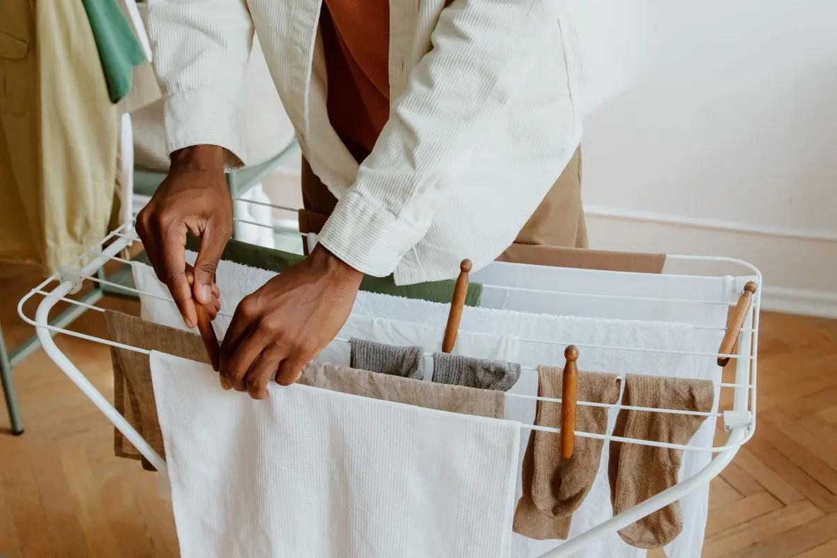 Hands spread a damp white shirt along the bars of a folding drying rack
