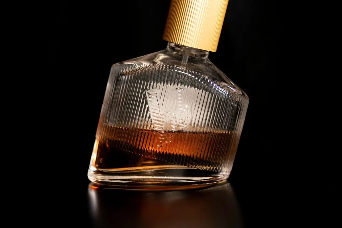 An amber cologne bottle with a gold cap, lit against a black background