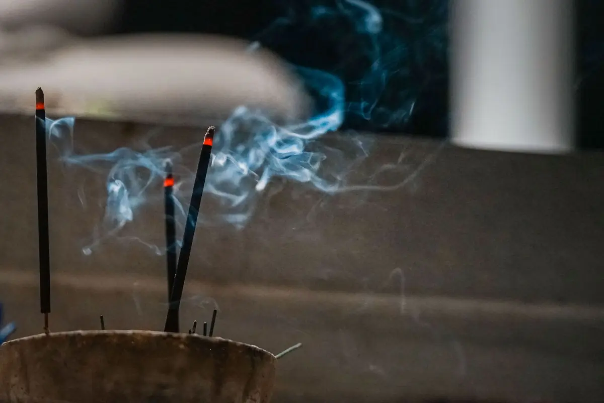 Two lit incense sticks send thin trails of smoke up from a holder
