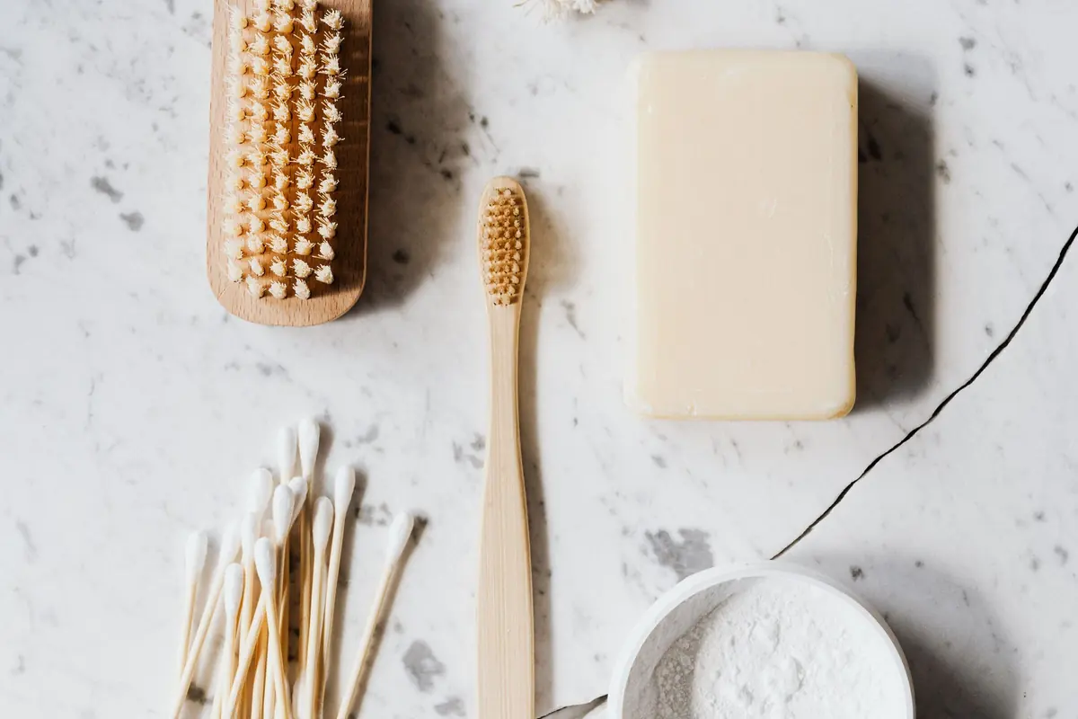 A scrubbing brush, a bamboo toothbrush, cotton buds, soap and a bowl of white powder on marble