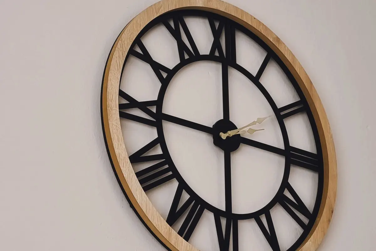 A simple black-and-white wall clock with Roman numerals on a pale wall