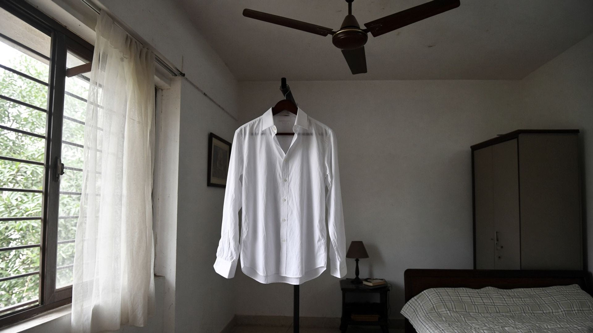 A freshly ironed white shirt on a hanger in humid morning light, already slightly limp before it is worn