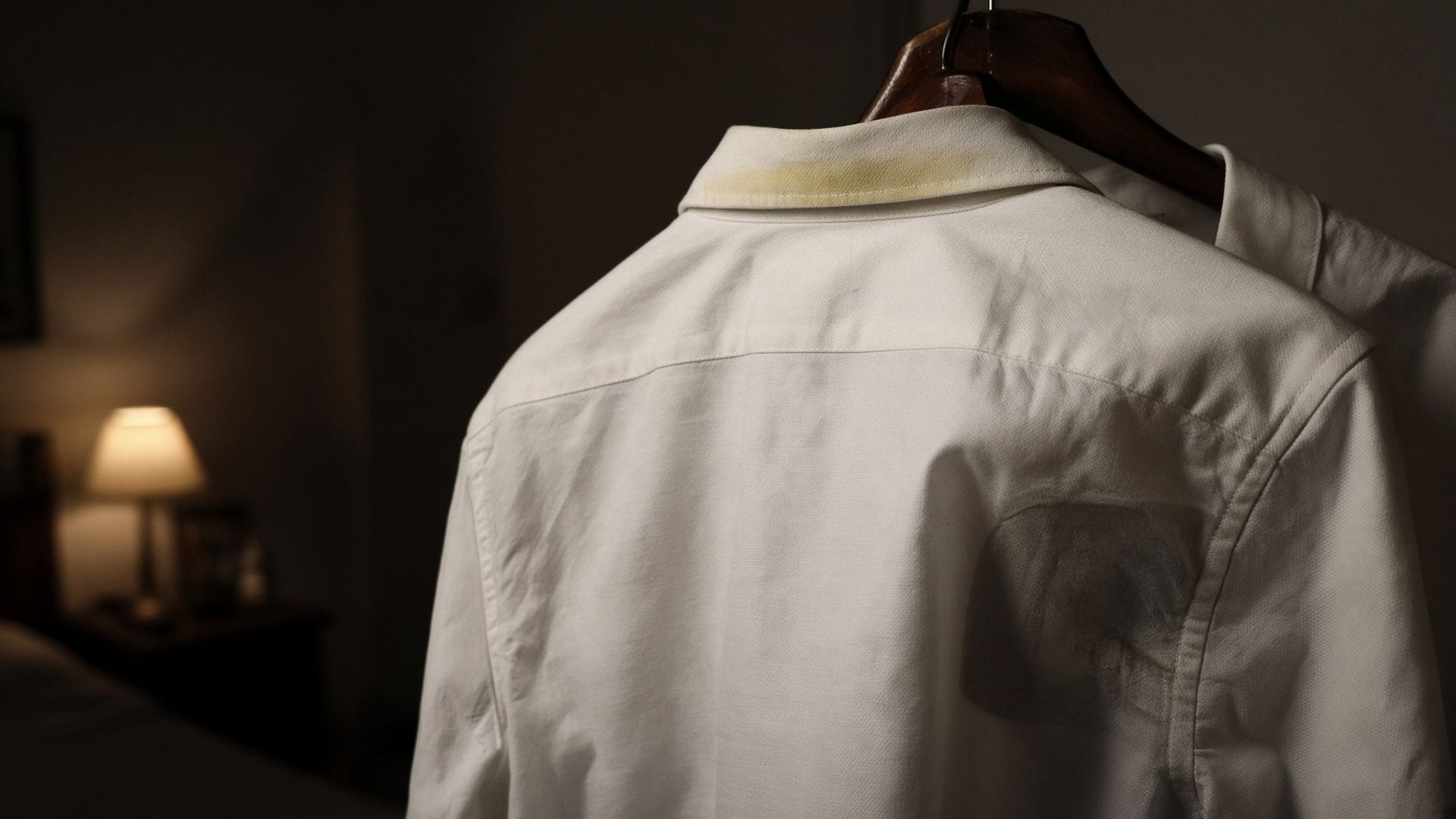 Close-up of a white office shirt on a hanger, inner collar band faintly yellowed and the underarm panel worn